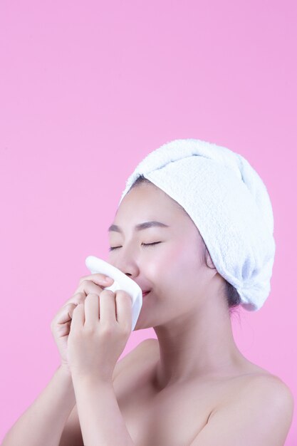 Mujer hermosa asiática que limpia la cara en un fondo, una cosmetología y un balneario rosados.