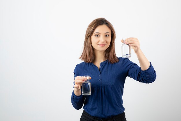 Mujer hermosa en blusa azul con vaso de agua sobre fondo blanco.