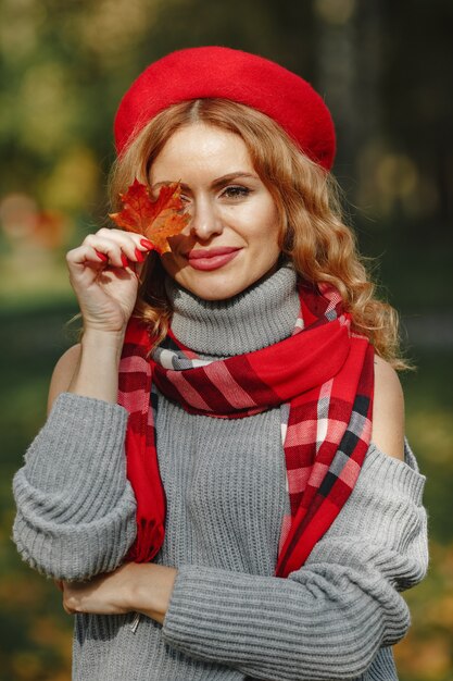 Mujer hermosa en una boina roja sostenga la hoja otoñal en la mano.