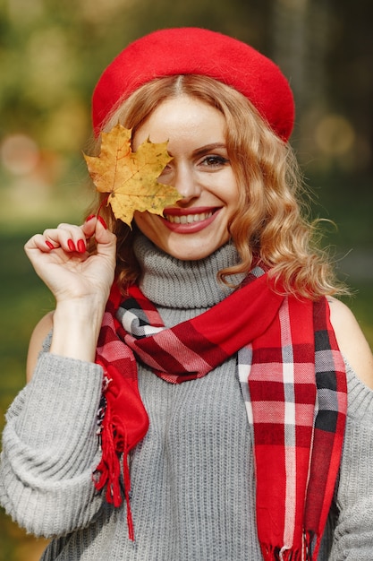 Mujer hermosa en una boina roja sostenga la hoja otoñal en la mano.