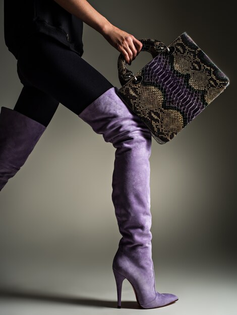 Mujer hermosa en botas altas de color púrpura. Chica de moda tiene elegante bolso de cuero violeta. Concepto de glamour elegante. Arte. Modelo camina después de ir de compras.