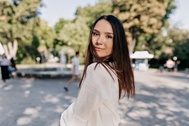 Una mujer hermosa con cabello oscuro posa con entusiasmo mientras camina por el parque