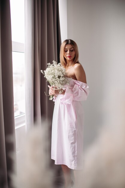 Mujer hermosa con cabello rubio medio mirando su boquet de flores blancas