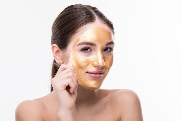 Mujer hermosa con la cara del tacto cosmético de la piel de oro aislada en la pared blanca. Belleza Cuidado de la piel y tratamiento