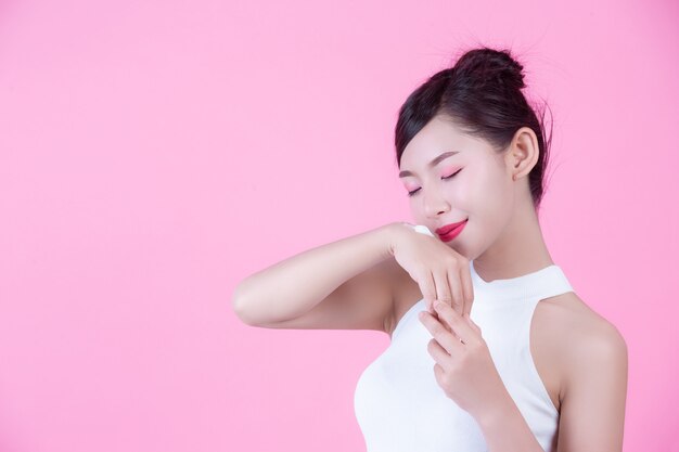 Mujer hermosa con crema en la piel en un fondo rosado.