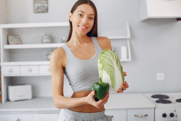 Mujer hermosa y deportiva en una cocina con verduras