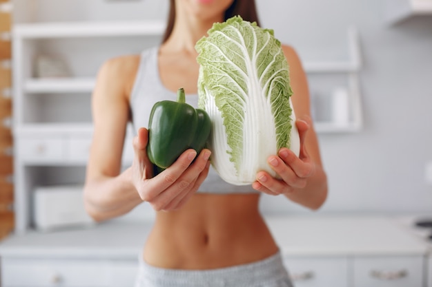 Mujer hermosa y deportiva en una cocina con verduras