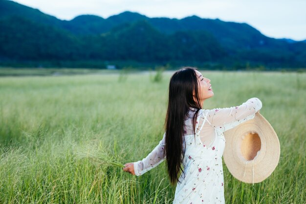 Una mujer hermosa y feliz está arrojando su sombrero en un hermoso prado y hay una montaña en el.