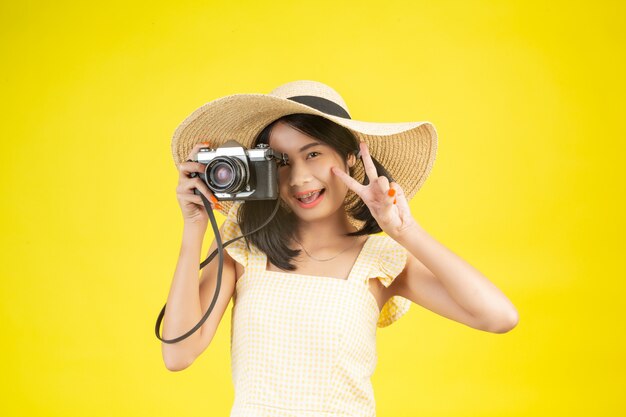 Una mujer hermosa y feliz con un gran sombrero y una cámara en un amarillo.