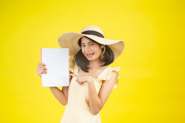 Una mujer hermosa y feliz con un gran sombrero y sosteniendo un libro blanco sobre un amarillo.