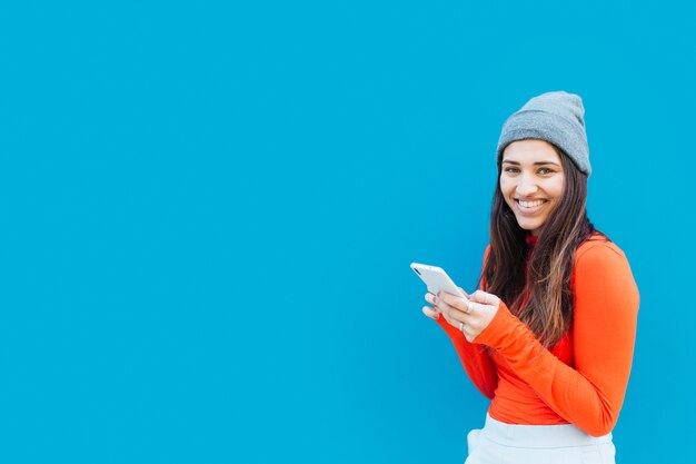 Mujer hermosa feliz que sostiene el teléfono móvil contra fondo azul