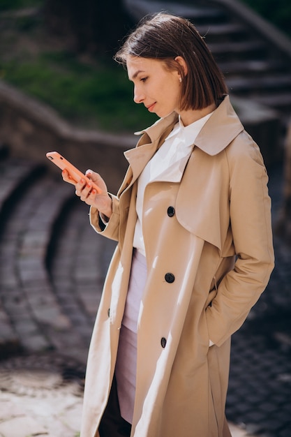 Mujer hermosa joven con abrigo caminando en la ciudad y hablando por teléfono