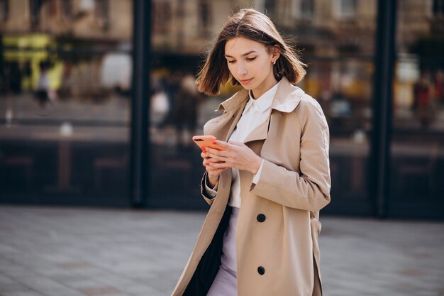 Mujer hermosa joven con abrigo caminando en la ciudad y hablando por teléfono