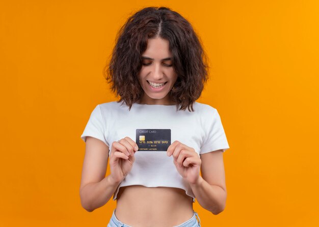 Mujer hermosa joven alegre que sostiene la tarjeta en la pared anaranjada aislada con el espacio de la copia