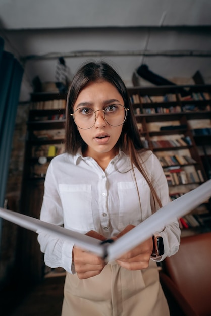 Mujer hermosa joven en anteojos parece sorprendida después de leer un libro