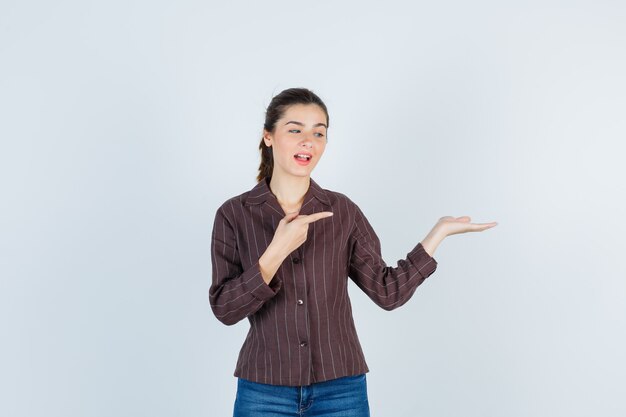 Mujer hermosa joven apuntando hacia la derecha, extendiendo la palma hacia un lado en la chaqueta y mirando feliz. vista frontal.