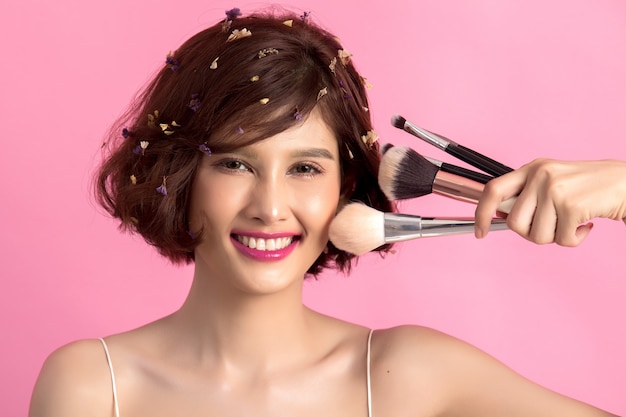 Mujer hermosa joven asiática del pelo corto que aplica el cepillo cosmético del polvo