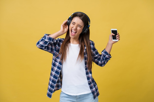 Mujer hermosa joven con auriculares bailando y cantando aislado sobre fondo amarillo.