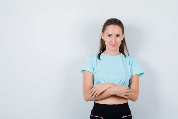 Mujer hermosa joven con los brazos cruzados en camiseta y mirando alegre, vista frontal.