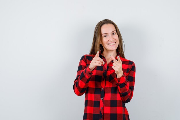 Mujer hermosa joven en camisa casual apuntando a la cámara y mirando contento, vista frontal.