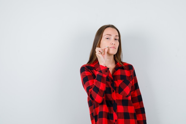 Mujer hermosa joven en camisa casual con los dedos cerca de la boca y mirando triste, vista frontal.