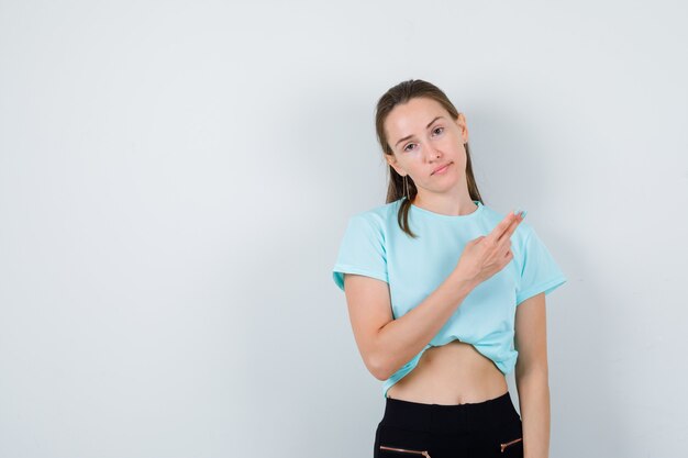 Mujer hermosa joven en camiseta apuntando a la esquina superior derecha y mirando triste, vista frontal.