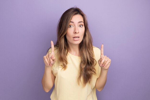 Mujer hermosa joven en camiseta beige mirando a la cámara con expresión de confianza en la cara inteligente