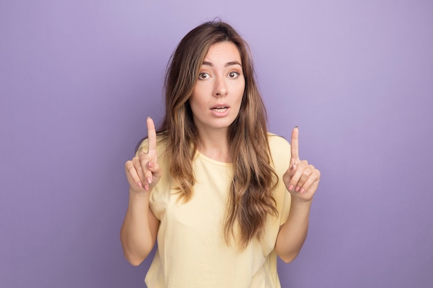 Mujer hermosa joven en camiseta beige mirando a la cámara con expresión de confianza en la cara inteligente