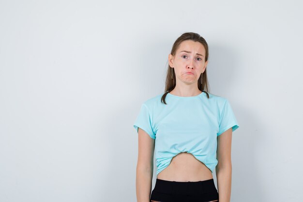 Mujer hermosa joven en camiseta mirando a cámara y mirando gruñón, vista frontal.