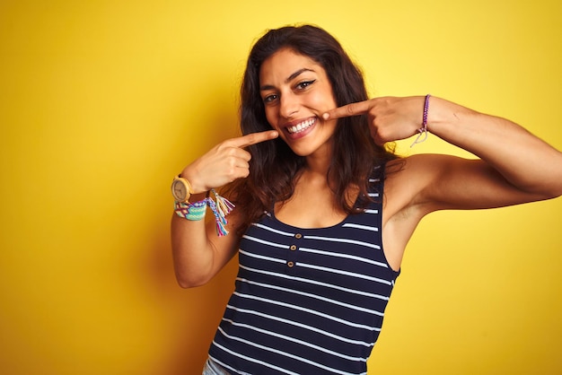 Mujer hermosa joven con camiseta a rayas de pie sobre un fondo amarillo aislado sonriendo alegre mostrando y señalando con los dedos los dientes y la boca Concepto de salud dental