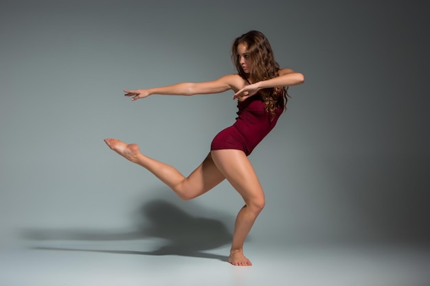 Mujer hermosa joven en camiseta roja y pantalones cortos bailando sobre un fondo de estudio gris oscuro. Moderno, Contemporáneo, improvisación