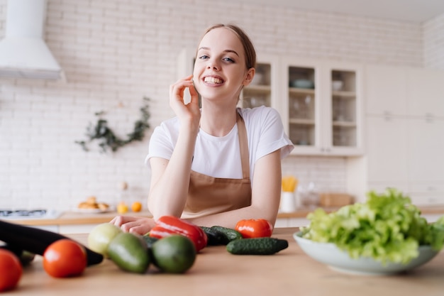 Mujer hermosa joven en la cocina en un delantal y verduras frescas sobre la mesa