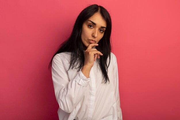 Mujer hermosa joven confiada que lleva la camiseta blanca que pone la mano en la barbilla