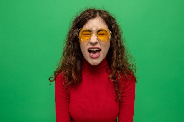 Foto gratuita mujer hermosa joven en cuello alto rojo con gafas amarillas gritando estar frustrado y emocionado