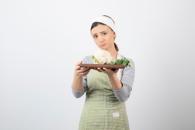 Mujer hermosa joven en delantal con plato de coliflor