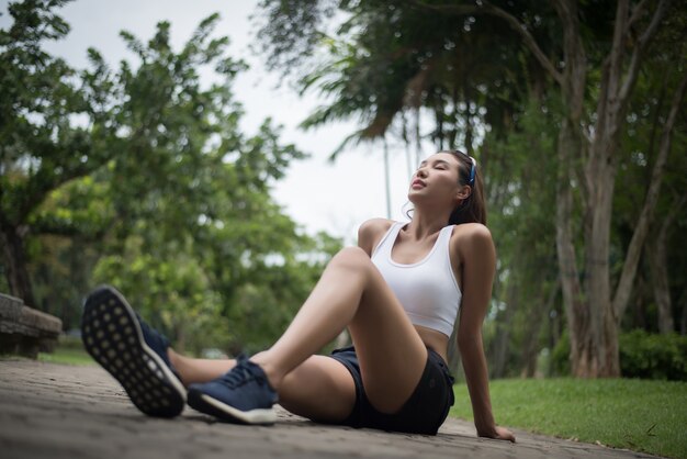 La mujer hermosa joven del deporte se sienta en el parque después de la sacudida. Concepto de salud y deporte.