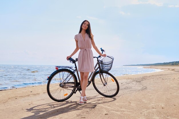 Mujer hermosa joven está disfrutando del verano con su bicicleta en la playa en el día soleado.