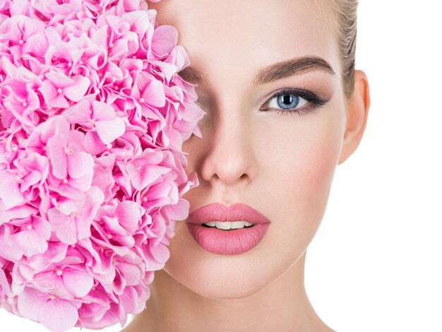 Mujer hermosa joven con flores junto a la cara.