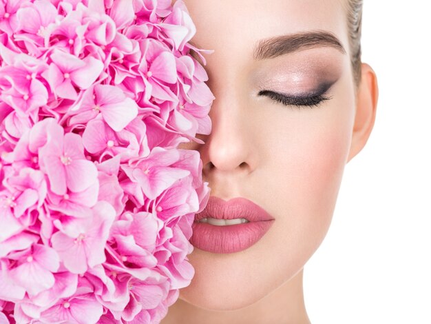 Mujer hermosa joven con flores junto a la cara.