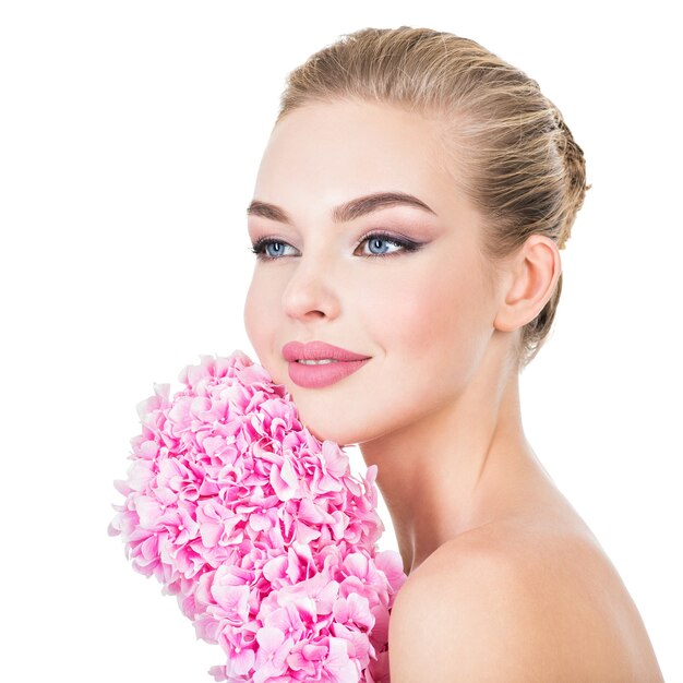 Mujer hermosa joven con flores junto a la cara.