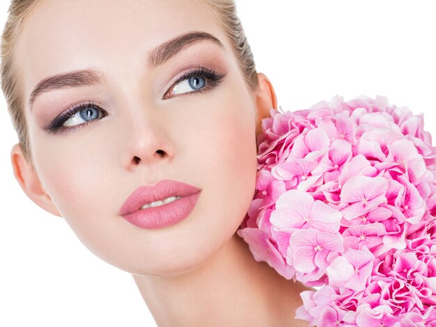 Mujer hermosa joven con flores junto a la cara.