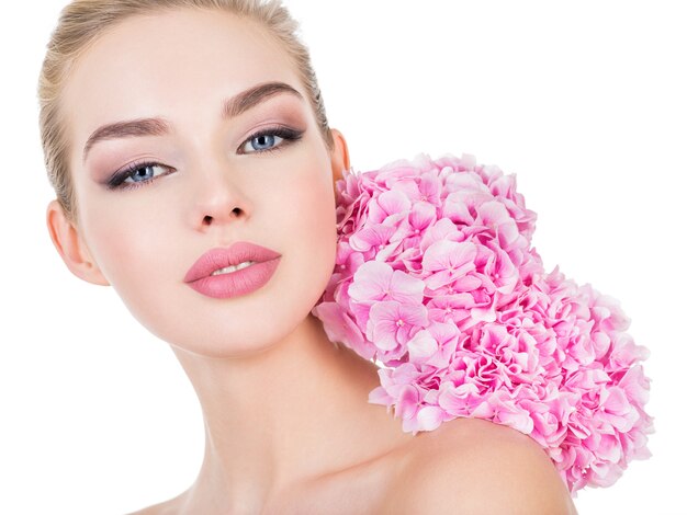 Mujer hermosa joven con flores junto a la cara.