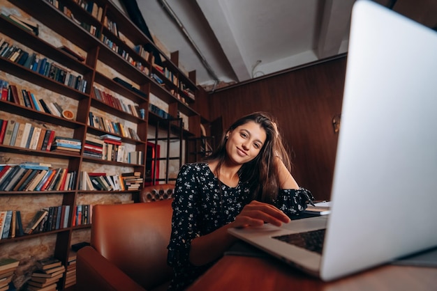 Mujer hermosa joven en gafas trabaja en la computadora portátil mientras está sentado en la mesa