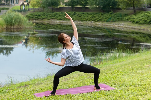 Mujer hermosa joven haciendo ejercicio de yoga en el parque verde