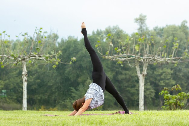 Mujer hermosa joven haciendo ejercicio de yoga en el parque verde