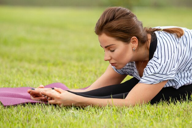 Mujer hermosa joven haciendo ejercicio de yoga en el parque verde