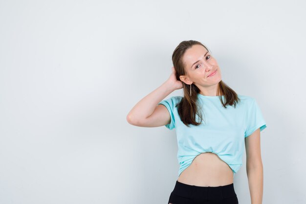 Mujer hermosa joven con la mano detrás de la cabeza en camiseta y mirando dichosa, vista frontal.