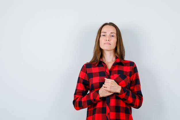 Mujer hermosa joven con las manos delante de ella en camisa casual y mirando confiada. vista frontal.