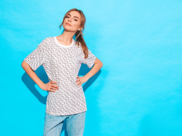 Mujer hermosa joven mirando a cámara. Chica de moda en ropa casual de verano camiseta amarilla. La hembra positiva muestra emociones faciales. Modelo divertido aislado en azul