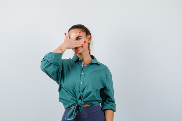 Mujer hermosa joven mirando a través de los dedos en camisa verde y mirando alegre. vista frontal.